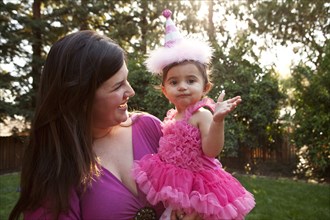 Mother holding daughter in party hat in backyard