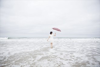 Woman wading with umbrella on beach