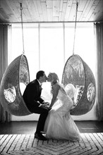 Caucasian bride and groom kissing in hanging chairs