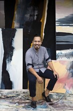 Pacific Islander artist sitting with paintings