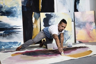 Pacific Islander artist kneeling on floor painting on canvas
