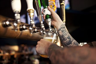Tattoos on arm of bartender pouring beer