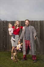 Caucasian couple posing near wooden fence with baby daughter