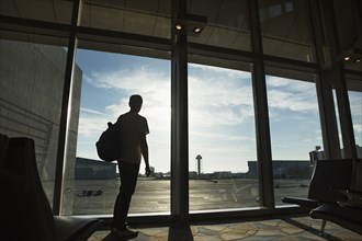 Silhouette of man looking out airport window