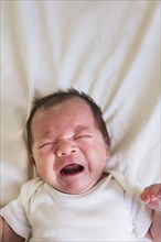 Close up of mixed race baby crying on bed