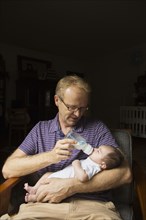 Father bottle feeding baby in armchair