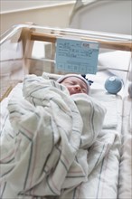 Mixed race wrapped in blanket in hospital crib
