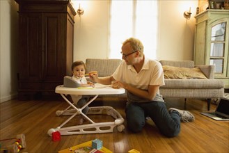 Father feeding son in high chair in living room