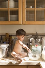 Mixed Race boy sitting on kitchen counter mixing food in bowl