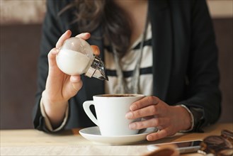 Woman sprinkling sugar in coffee in cafe