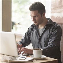 Man using laptop with cup of coffee in cafe