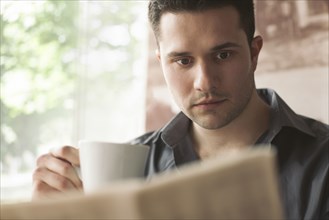 Man drinking cup of coffee and reading newspaper