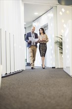 Caucasian business people reading paperwork in office corridor