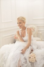 Smiling bride sitting with bouquet on bed