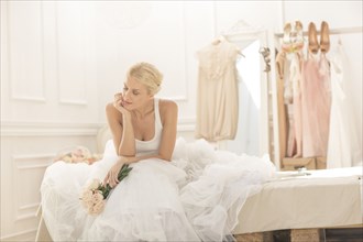 Pensive bride sitting with bouquet on bed