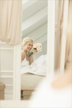 Smiling bride admiring herself in mirror on bed