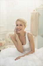 Smiling bride talking on cell phone on bed
