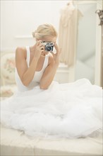 Bride photographing with vintage camera on bed