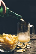 Hand pouring glass of beer near potato chips