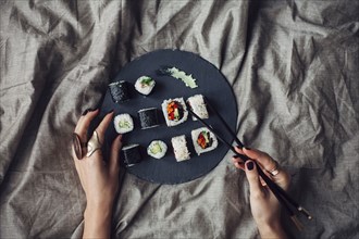 Hands of woman reaching for platter of sushi on bed