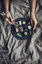 Woman eating sushi with chopsticks in bed