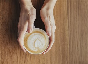 Hands holding cup of coffee with leaf drawn in milk