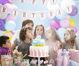 Children blowing out candles on birthday cake in party