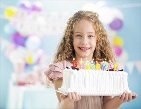 Smiling girl holding birthday cake at party