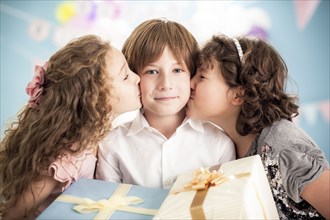Girls kissing cheeks of boy at birthday party