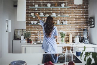 Caucasian woman reaching for dishes in kitchen