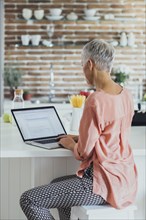 Older Caucasian woman using laptop in kitchen