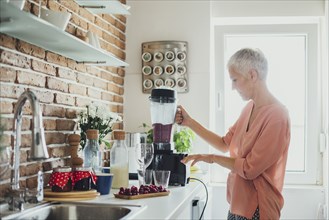 Older Caucasian woman blending smoothie in kitchen