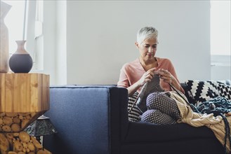 Older Caucasian woman knitting on sofa