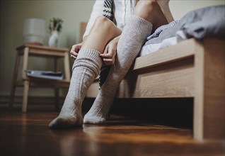 Caucasian woman sitting on bed pulling up socks