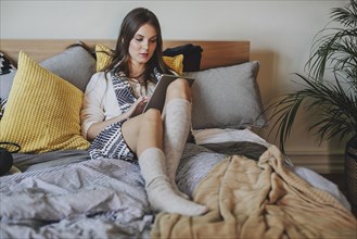 Woman reading digital tablet on bed