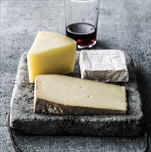 Variety of wedges of cheese on cutting board with red wine