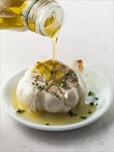 Bottle pouring olive oil on roasted garlic