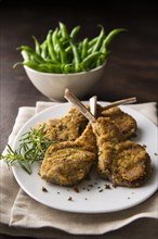 Breaded lamb chops on plate with bowl of green beans