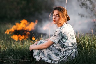 Caucasian woman sitting near fire in rural field