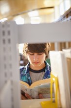Mixed race boy reading book in library