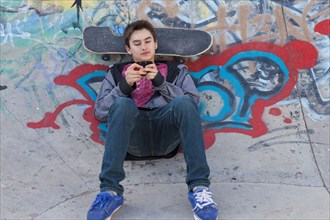 Mixed race boy with skateboard text messaging on cell phone