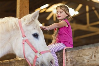 Caucasian girl petting horse in barn