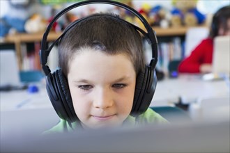 Caucasian student in headphones using laptop in classroom