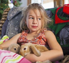 Caucasian girl holding pet rabbits on sofa