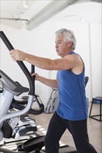 Older Hispanic man using elliptical machine in gym
