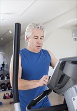 Older Hispanic man using elliptical machine in gym