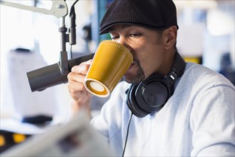 Mixed race disc jockey drinking cup of coffee in studio