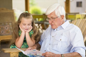 Caucasian man and granddaughter reading outdoors