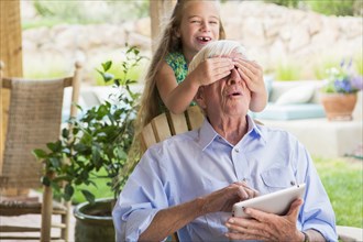 Caucasian girl covering grandfather's eyes on patio