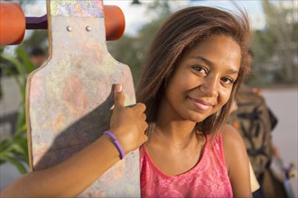 Mixed race teenage girl holding skateboard outdoors